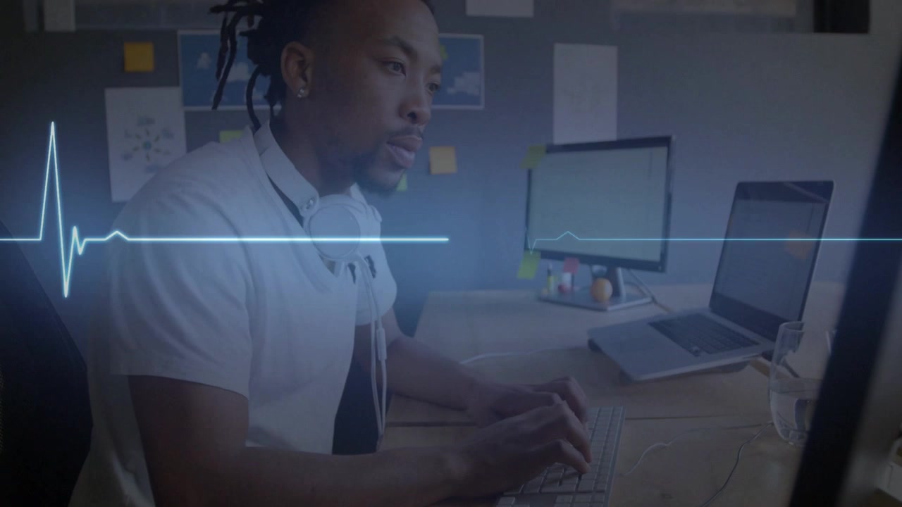 Adult male typing at tech desk, studying screens, heartbeat graphic pulsing with keystrokes
