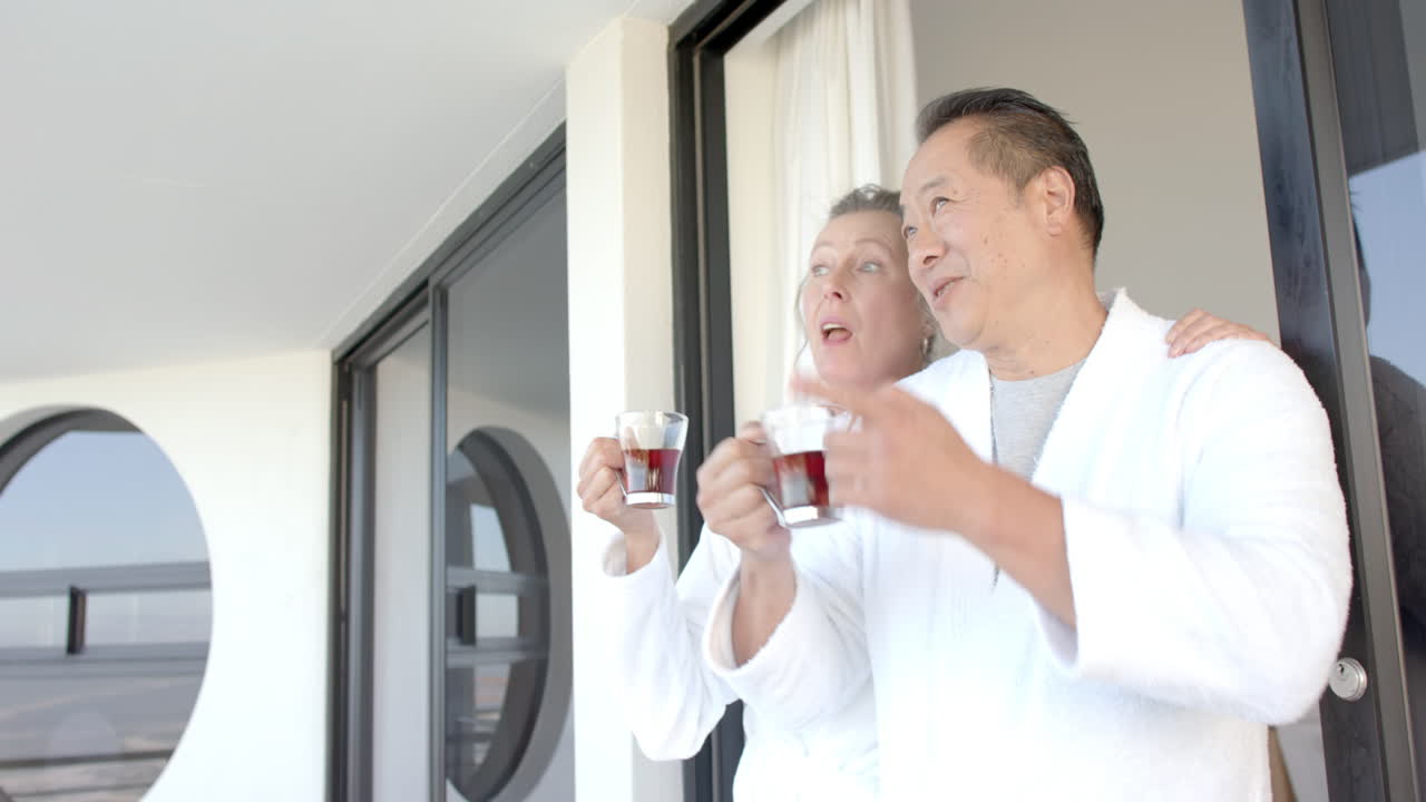 Senior couple in bathrobes enjoying drinks on balcony during vacation