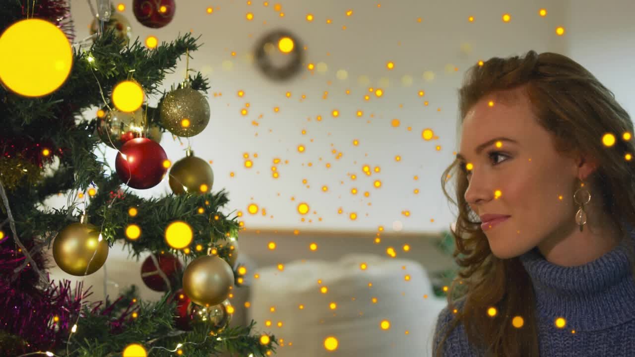 Mujer levantando una bola dorada para una campaña de decoración mientras anillos animados y destellos giran sobre el árbol