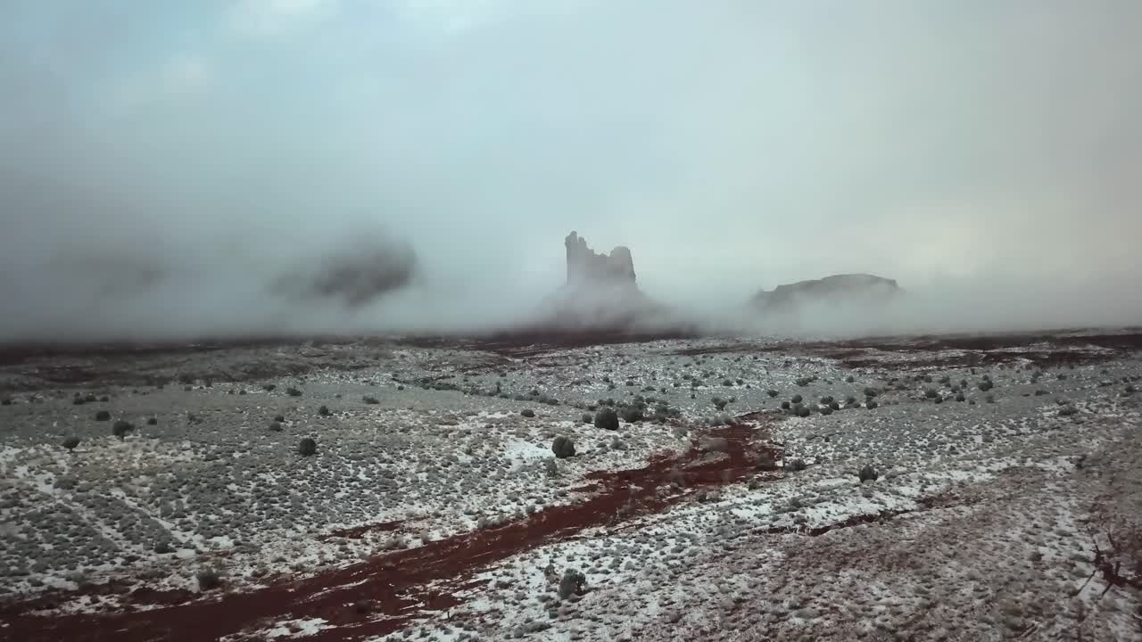 toma aérea que se inclina hacia arriba desde el suelo del desierto cubierto de nieve para revelar nubes bajas que cubren el horizonte montañoso de utah