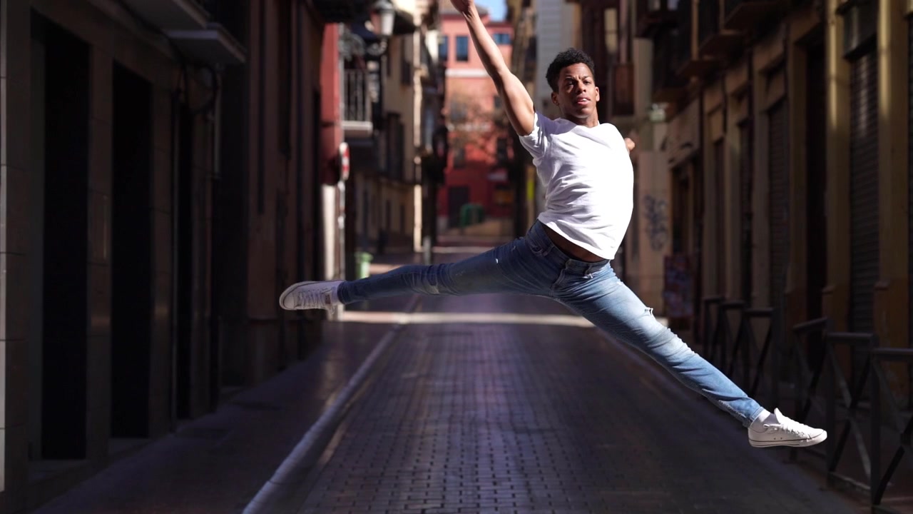 Giovane acrobata di colore che esegue un salto di balletto per strada.