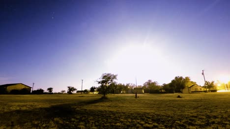 nightlapse - luna y estrellas en el cielo sobre un pequeño pueblo en el campo