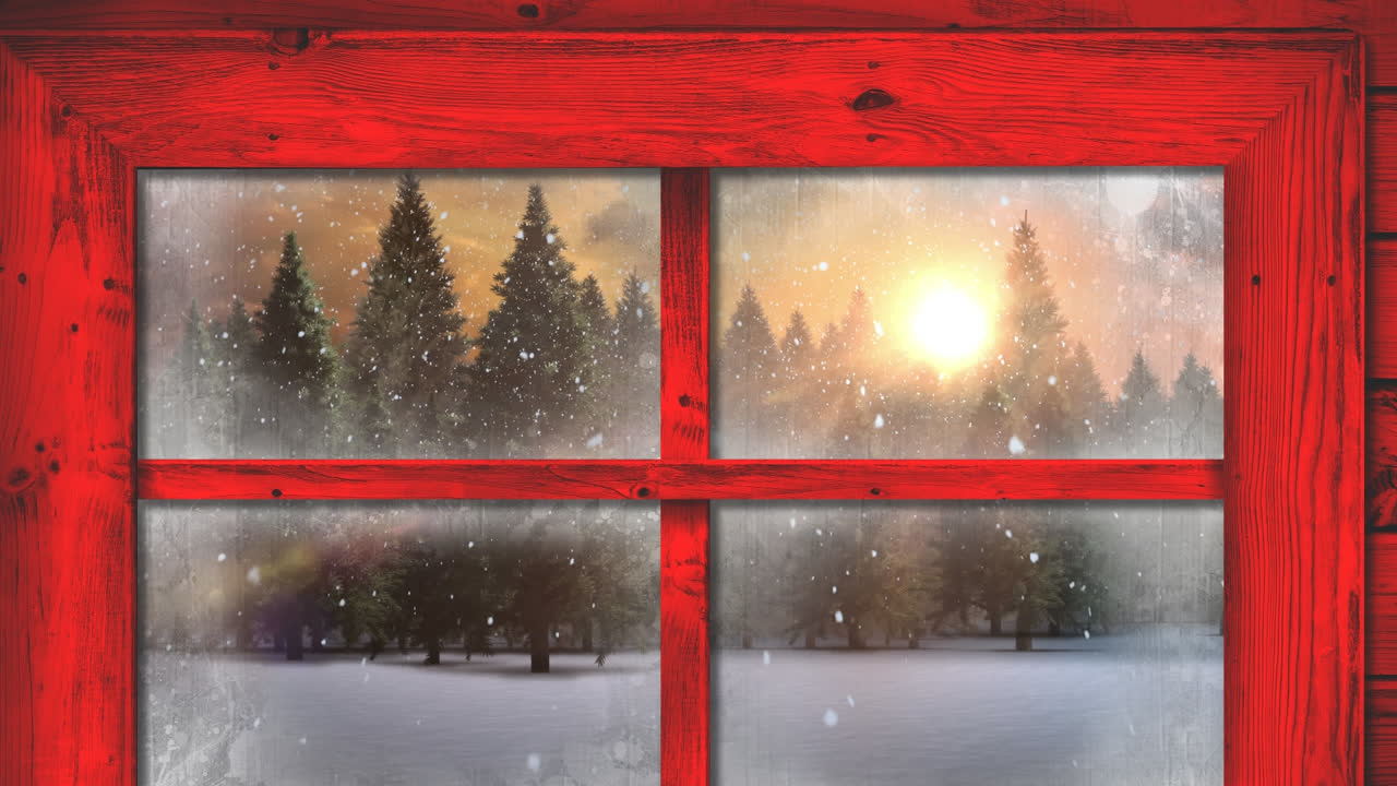 Red wooden window frame against snow falling over multiple trees on winter landscape