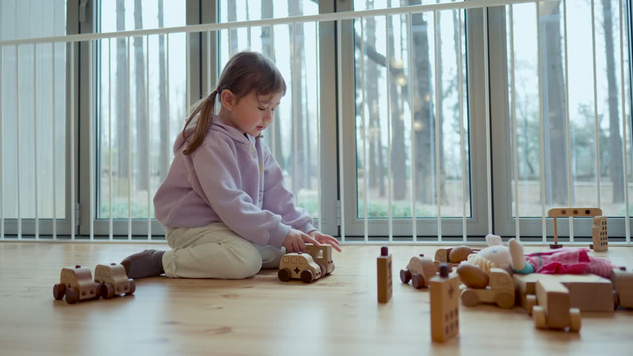 Young caucasian white child playing with wooden car toys on ground in a bright indoor playroom, exploring objects, creative playtime, low angle static