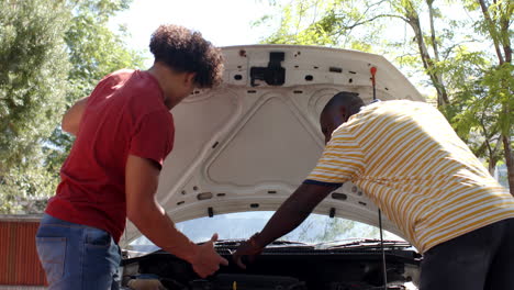 inspecting car engine, two multiracial male friends checking under hood in outdoor setting