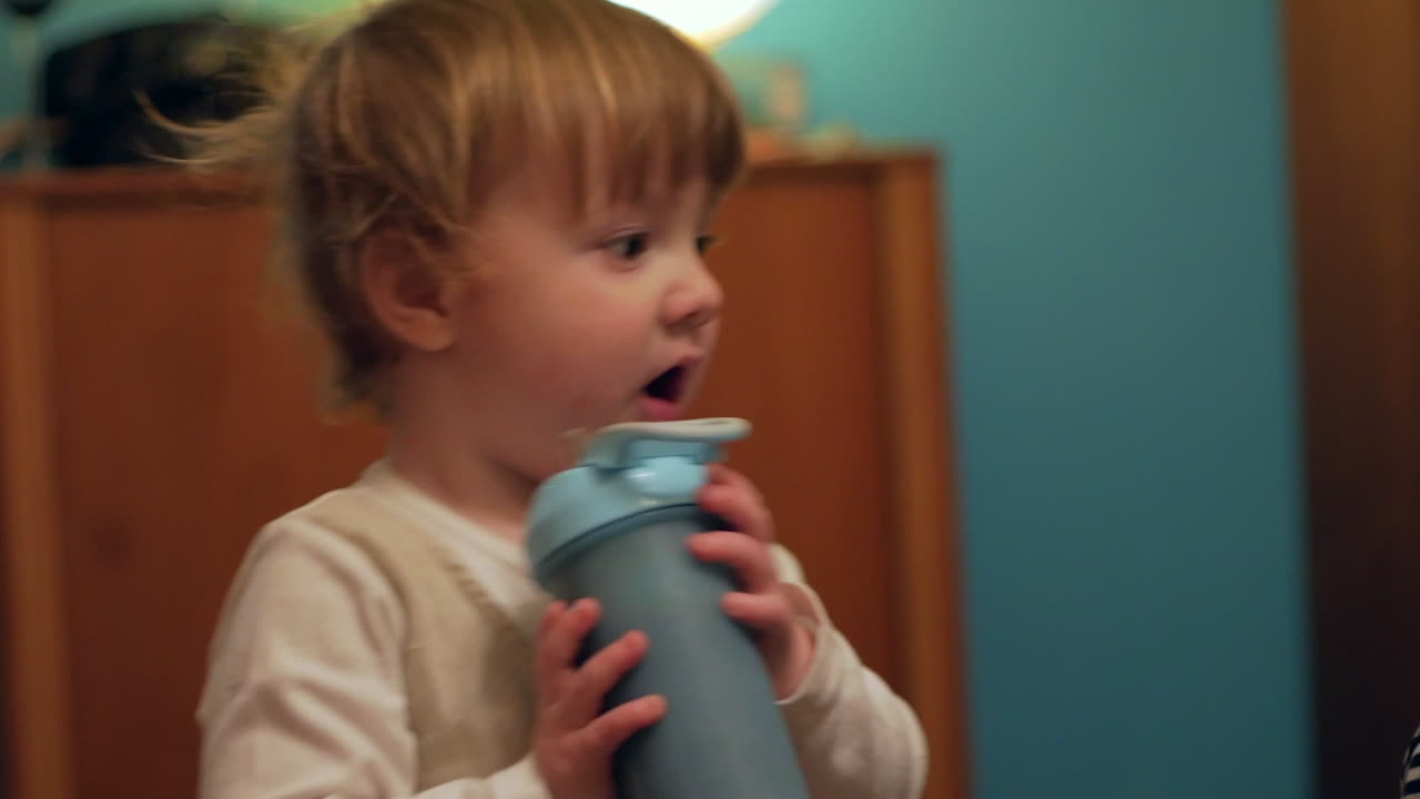 Un tenero bambino piccolo paffuto che beve un frullato da un contenitore blu mentre guarda i suoi genitori accanto a lui - Primo piano.
