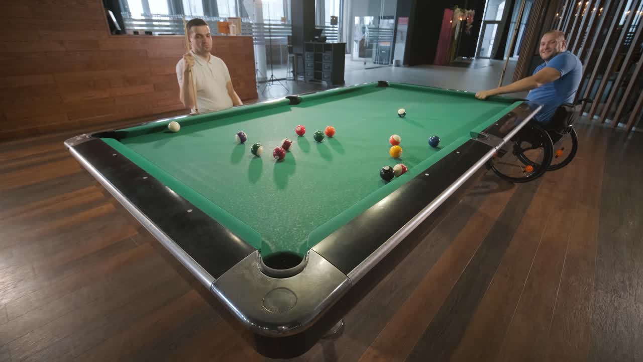 체어에 앉아 있는 장애인 성인 남성들이 클럽에서 빌리어드를 치고 있습니다.