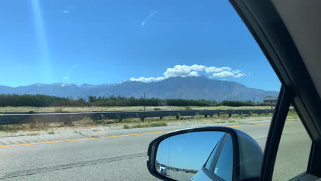 driving down highway looking out of the drivers  side window. blue skies with mountain in the background. light traffic.