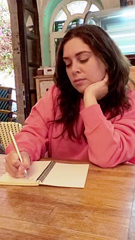 a woman in a pink sweater is writing in a notebook
