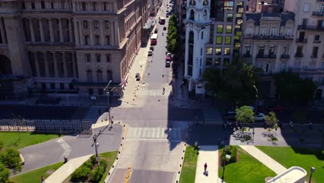 Aerial-view-dolly-in-of-people-passing-a-grated-on-the-street-of-Buenos-Aires-city,-characteristic-European-architecture,-sunny-day-slow-motion