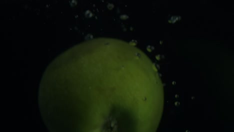 real time shot of falling green apple in water with bubbles in front of black blackground