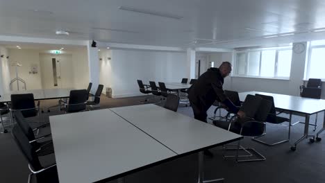 a man rearranges chairs around an office table, organizing them in batches and removing them, exemplifying the role of an office facilities worker