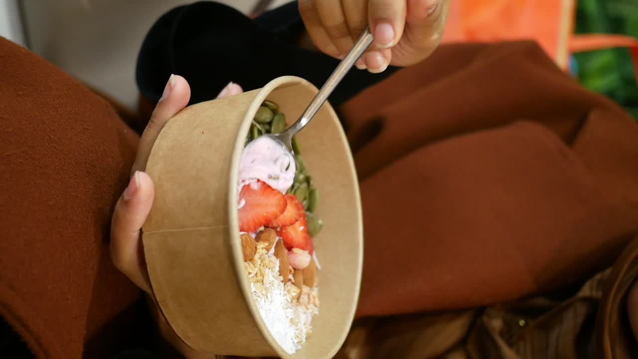 Person eating a yogurt bowl with granola, fruit, and nuts