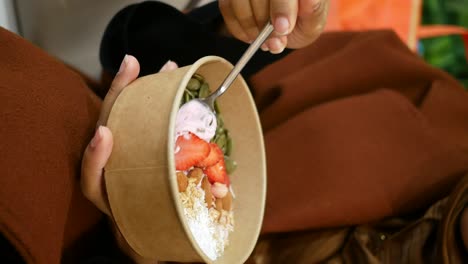 person eating a yogurt bowl with granola, fruit, and nuts