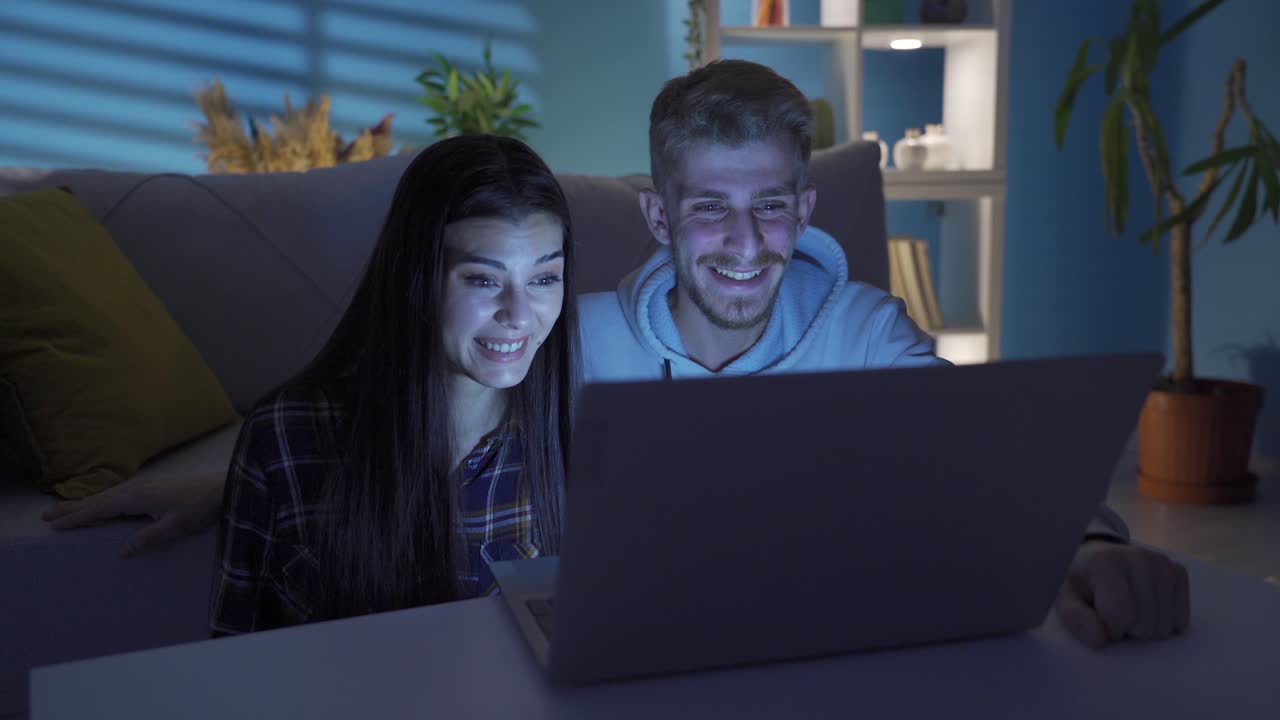 una joven pareja feliz viendo una película en su computadora portátil en casa.