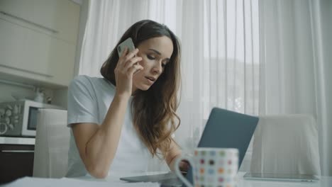 mujer freelance hablando por teléfono en la cocina de casa. persona femenina usando teléfono móvil