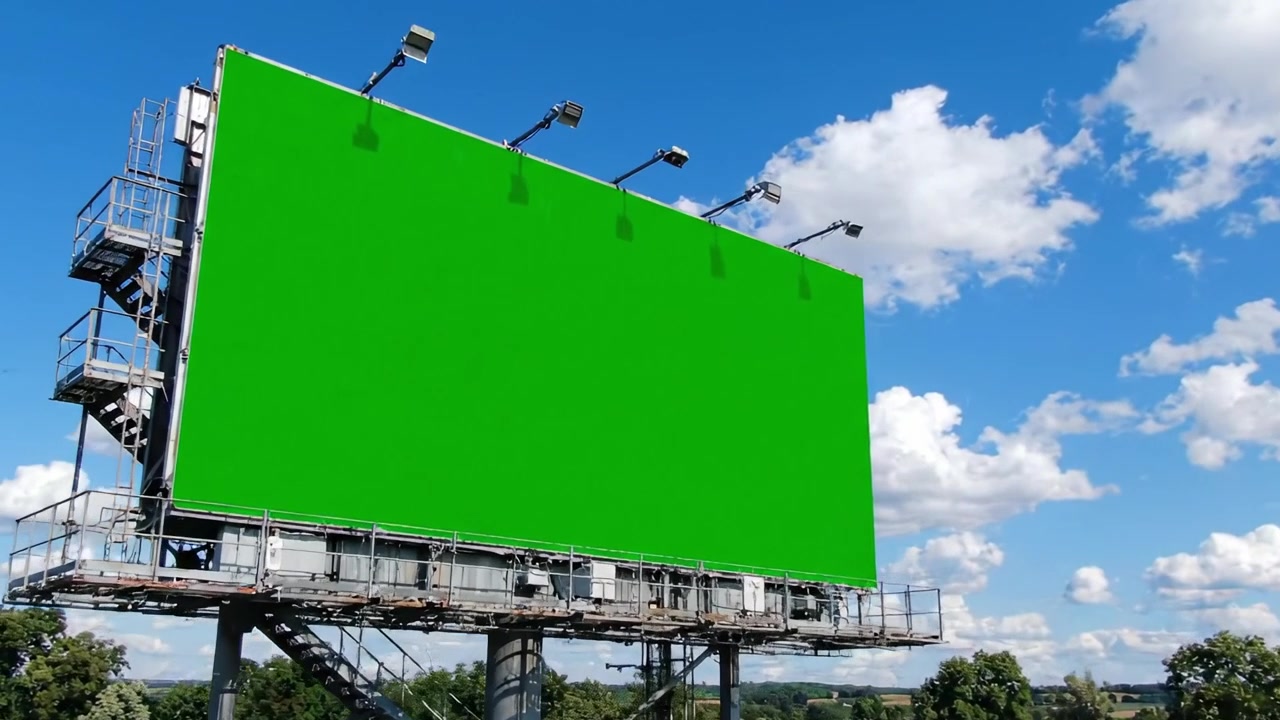 En panoramaudsigt over et stort grønt billboard under en klar blå himmel prydet med bløde hvide skyer, der fremhæver dets enorme reklamepotentiale for kreative kampagner.