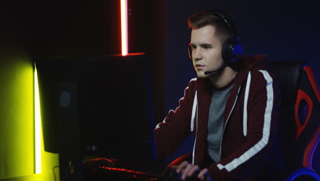 close up view of young serious man with headphones and playing a game on the computer in a room with colorful neon lamps on the wall 5