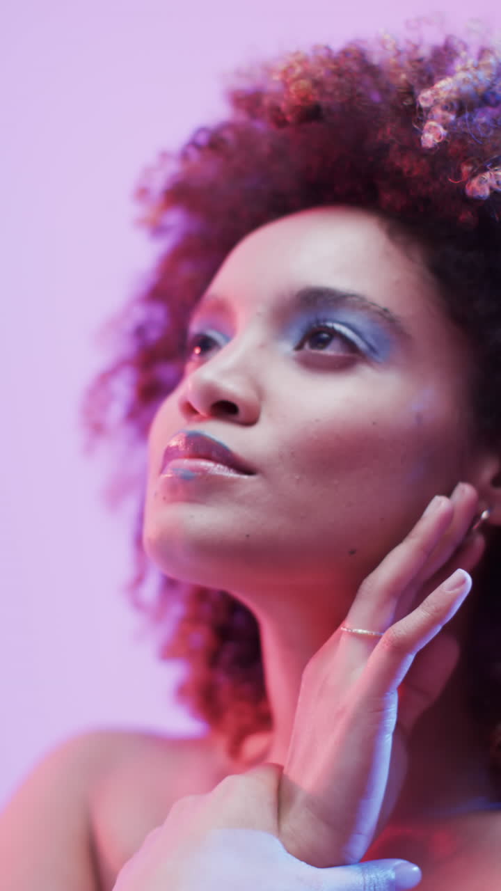 Vídeo vertical de mulher birracial com cabelo escuro em luz azul e rosa, em câmera lenta.
