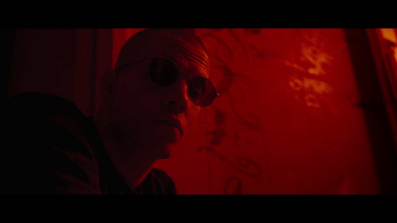 Man in profile view with glasses, in a dimly lit room with red walls