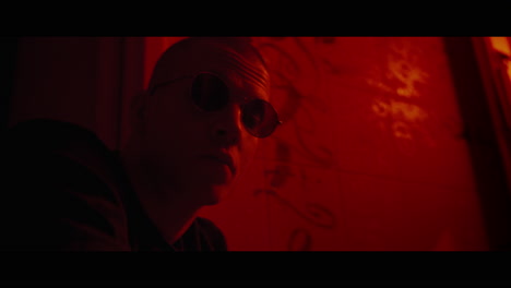 man in profile view with glasses, in a dimly lit room with red walls