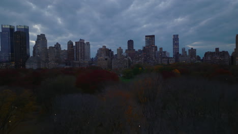 Los-Delanteros-Vuelan-Sobre-Los-árboles-De-Colores-Otoñales-En-El-Parque-Central-Al-Atardecer.-Vista-Panorámica-De-Edificios-De-Gran-Altura-Alrededor-Del-Parque-Urbano.-Manhattan,-Ciudad-De-Nueva-York,-Estados-Unidos