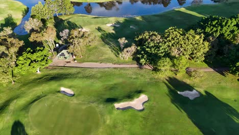 drone footage captures a lush golf course with vibrant greens, sand bunkers, and a serene water hazard under bright sunlight