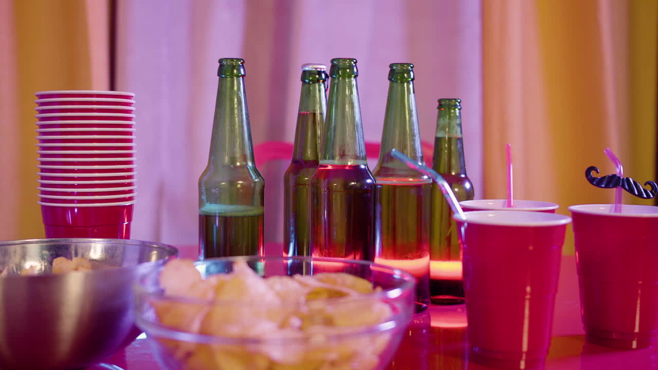 primer plano de papas fritas, botellas de cerveza y vasos de plástico en una mesa de fiesta en casa