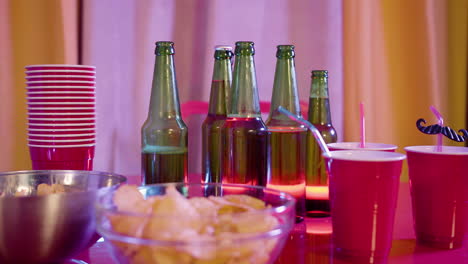 nahaufnahme von kartoffelchips, bierflaschen und plastikbechern auf einem partytisch zu hause