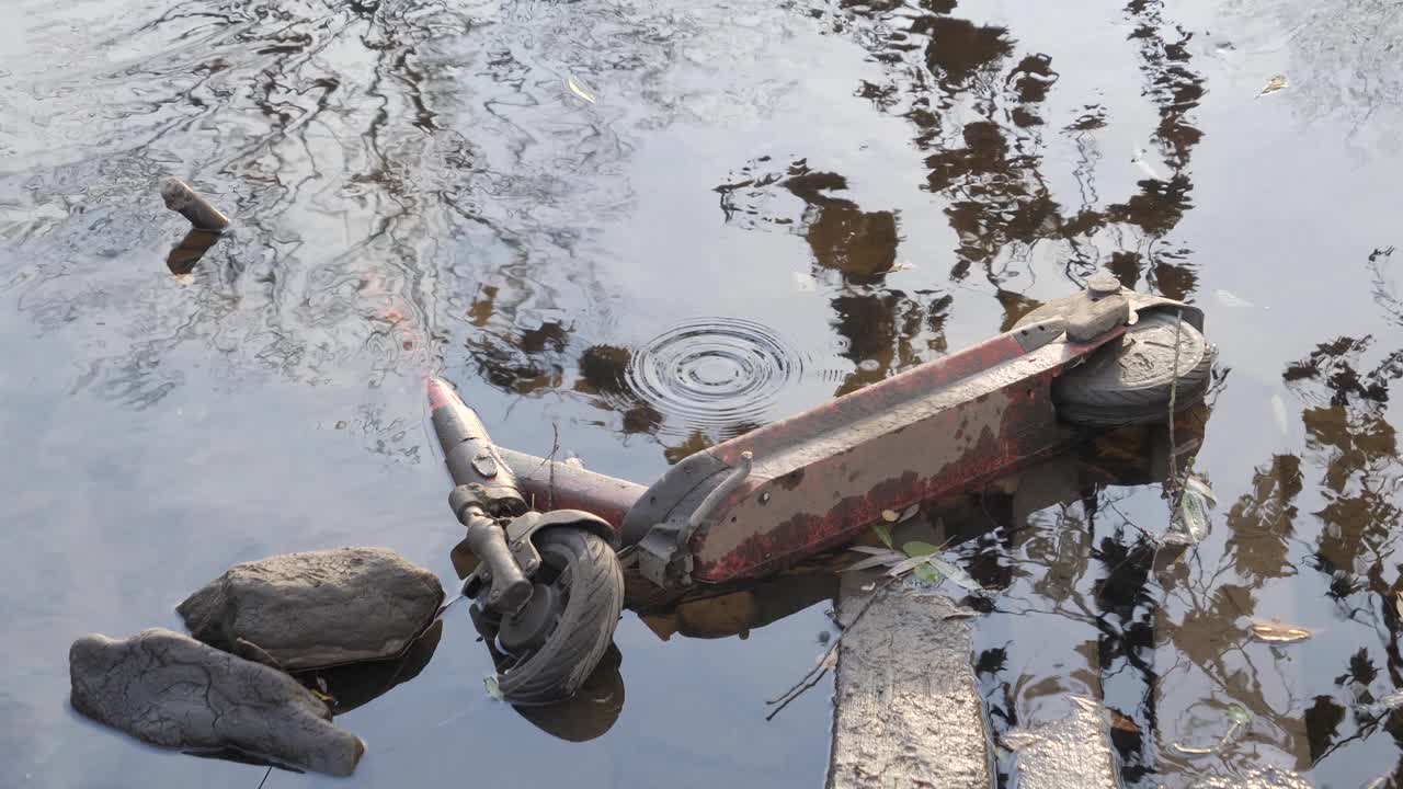 Old rusty kick scooter laying in a lake during the day, medium shot