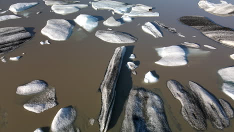 Toma-Aérea-De-Fondo-De-Muchos-Pedazos-De-Hielo-Rotos-De-Un-Glaciar-En-Agua-Marrón,-En-Islandia,-Heinabergsjökul