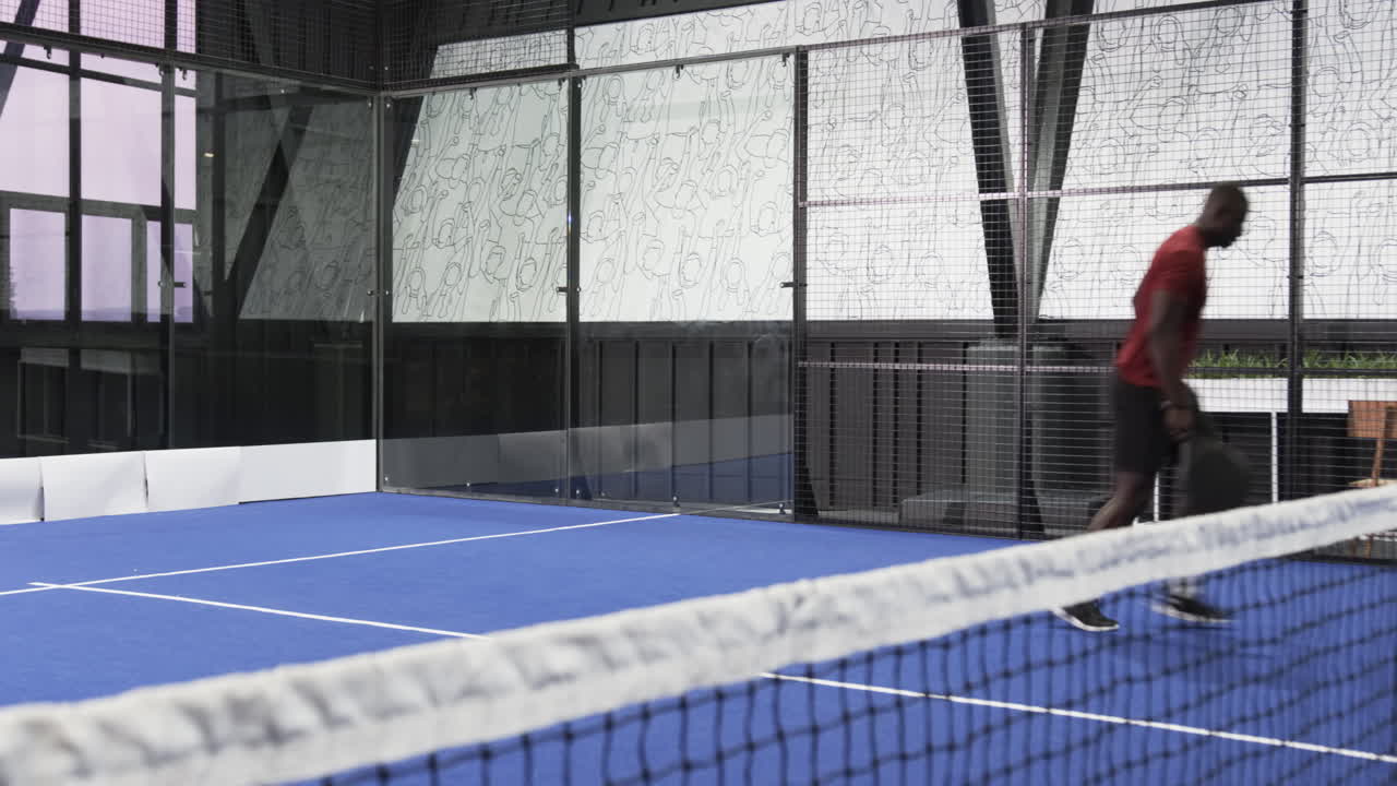 African American man playing padel tennis on indoor court, focused and ready