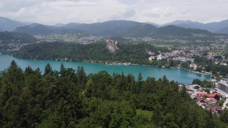 Toma-Aérea-Reveladora-De-Bosque-Verde-Con-Lago-Sangrado-Natural-Y-Cordillera-En-El-Fondo-Durante-El-Día-Nublado,-Eslovenia