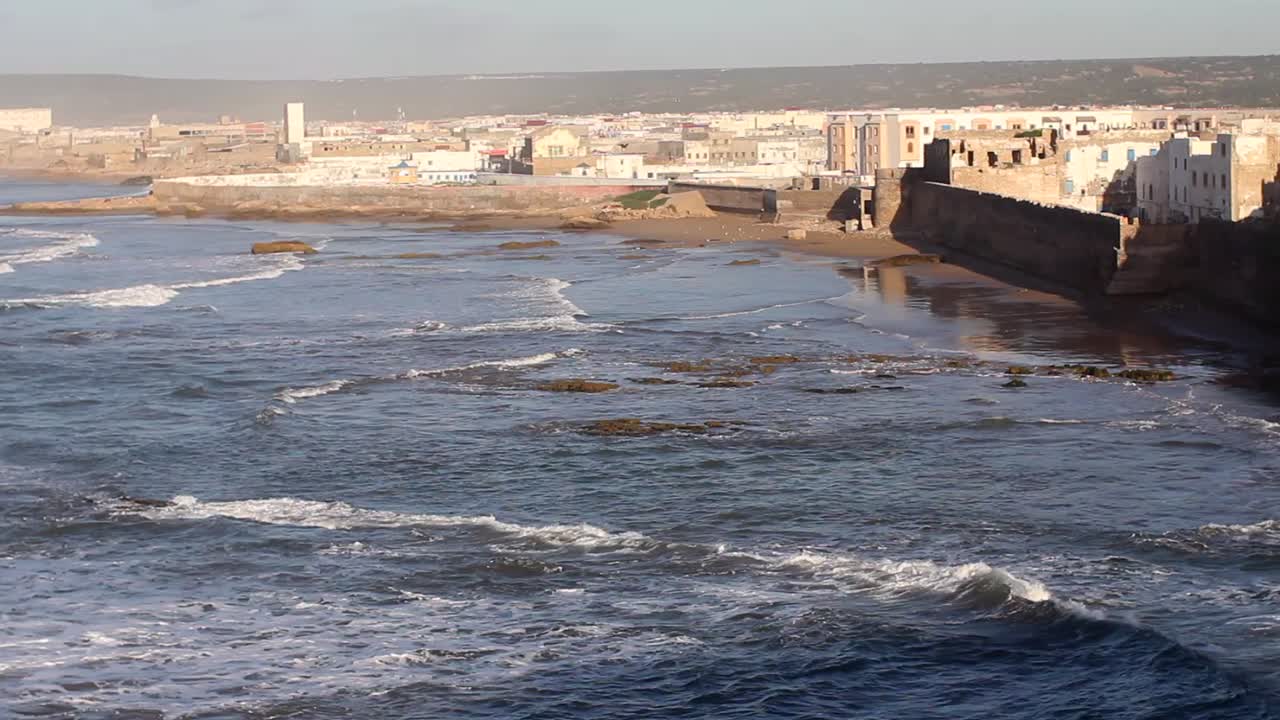 Panning to the right from Atlantic ocean with rollers coming in to the walls of Essaouira, Morocco