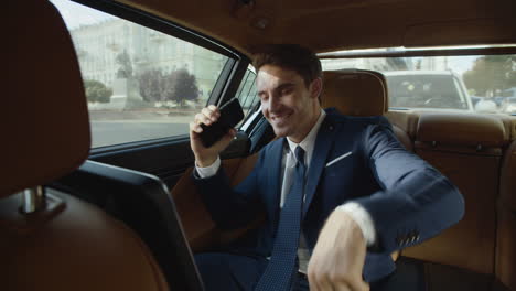 charming business man having fun with mobile phone in modern car. man in car