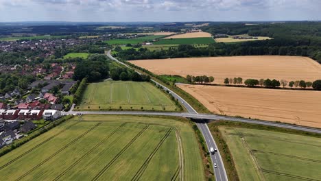 traffic on highway in suburb of american city during sunny day. aerial wide shot. agricultural farm fields and clouds at sky. american countryside with village.