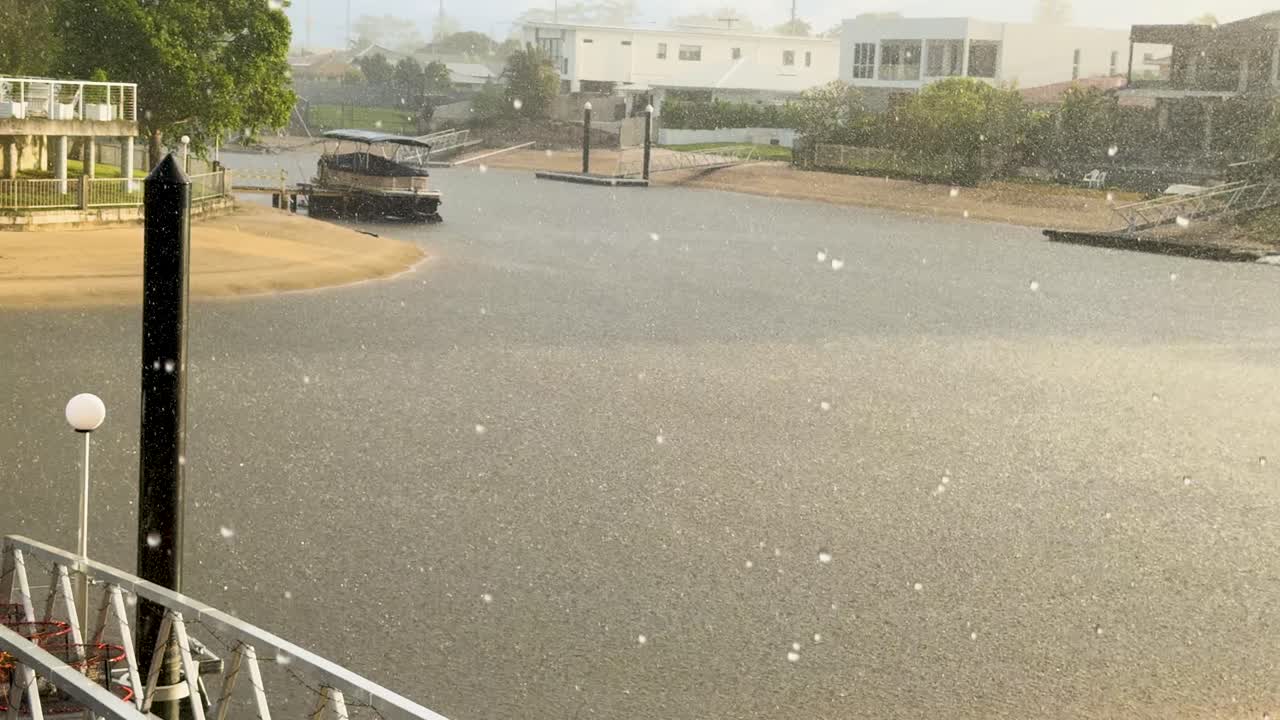 A serene canal scene with gentle rain and sunlight, showcasing luxury homes and boats in Gold Coast, Australia