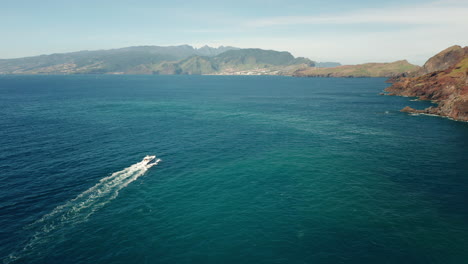 yacht travels in stunning turquoise water near shore of madeira, aerial