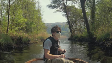 young man driving outboard lake boat wearing mask surrounded by nature