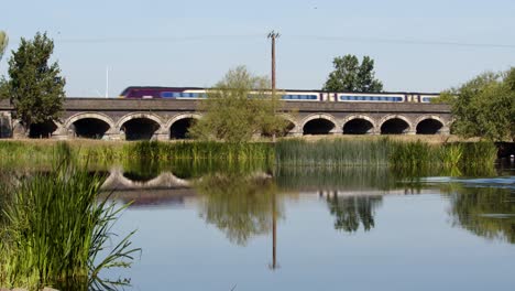 passenger train going over trent railway line bridge with river trent in foreground by ratcliffe on soar power station. wide shot
