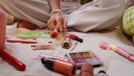 mujer sentada en una cama con maquillaje esparcido por ahí