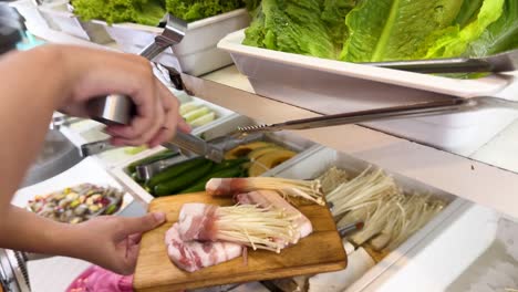 hands arrange pork and mushrooms for korean bbq. bright, natural lighting highlights fresh ingredients on a wooden board