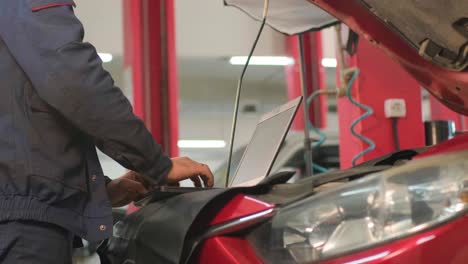 computer diagnostics of cars, young mechanic specialist male uses laptop technology while repairing vehicle with open hood at service station