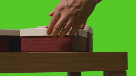 close up of man putting present into gift wrapped box on table shot against green screen