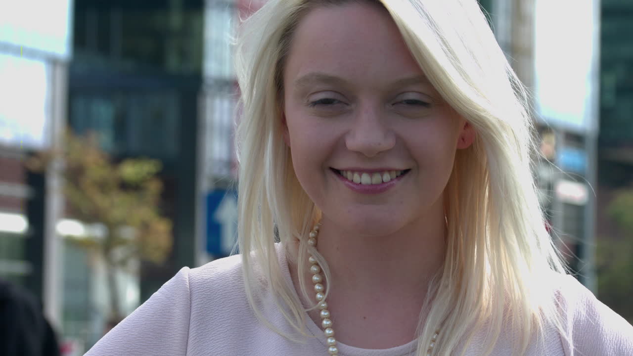 Close up of Happy blonde women smiling on the camera. Cheerful portrait of girl wearing pearl beads looking in the front with a smile on her face and city streets as background