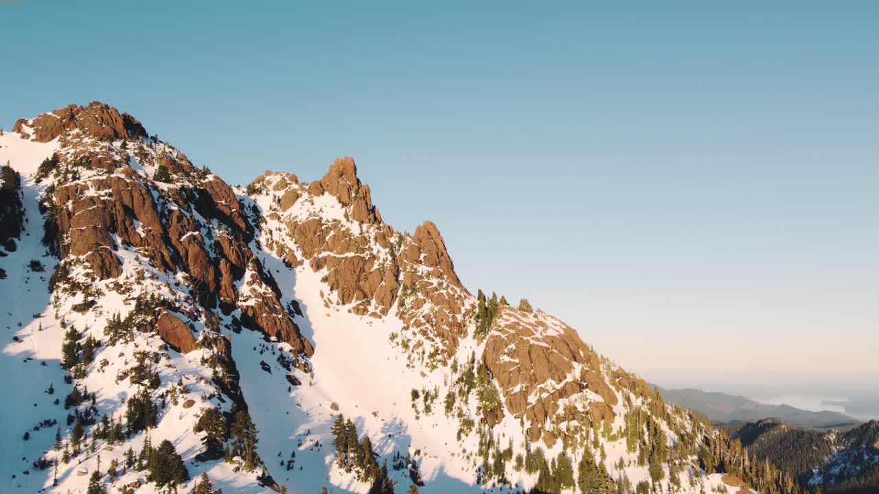 una toma ascendente de un dron de un pico nevado en las montañas olímpicas tomada desde las afueras del parque nacional al atardecer