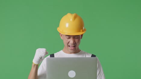 Close Up Of Asian Man Painter Wearing Safety Helmet Looking At The Laptop Then Screaming Goal Celebrating While Standing In The Green Screen Background Studio