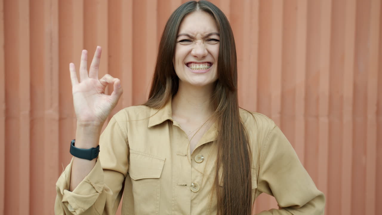 Woman wearing a jumpsuit, smiling and making an ok gesture.
