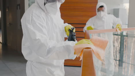 close up view of two cleaning men wearing personal protective equipment cleaning stair railings inside an office building