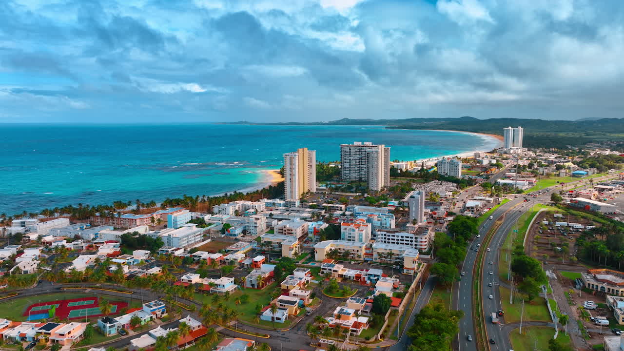 Paisaje urbano populoso, principalmente de baja altura, en la orilla del paisaje acuático azul. Un paisaje de nubes cubre el cielo sobre el paisaje marino y la costa. Puerto Rico, imágenes de dron